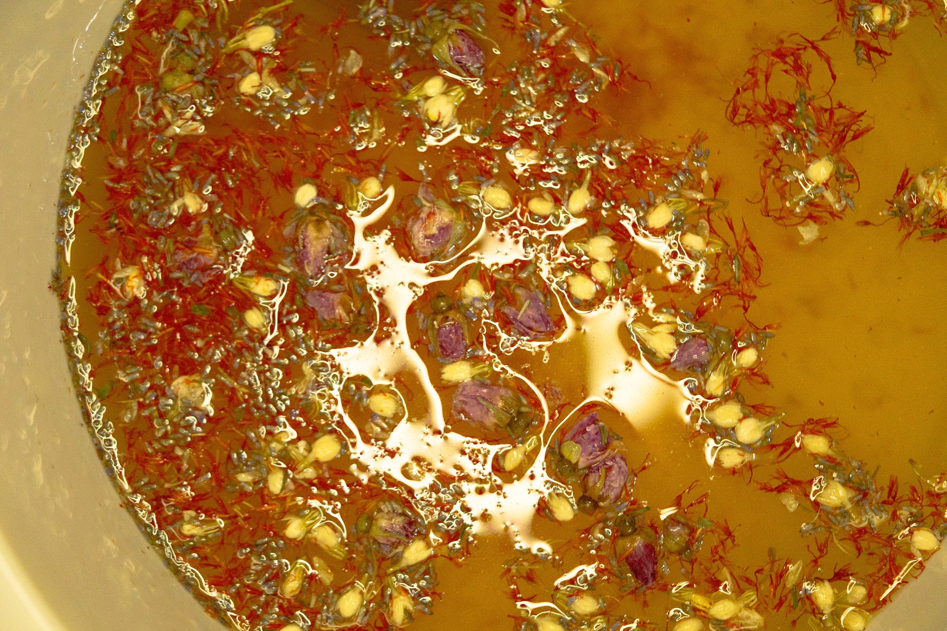 Close-up of botanical ingredients infusing in warm water during a herbal foot soak, showing floating petals and natural plant textures.