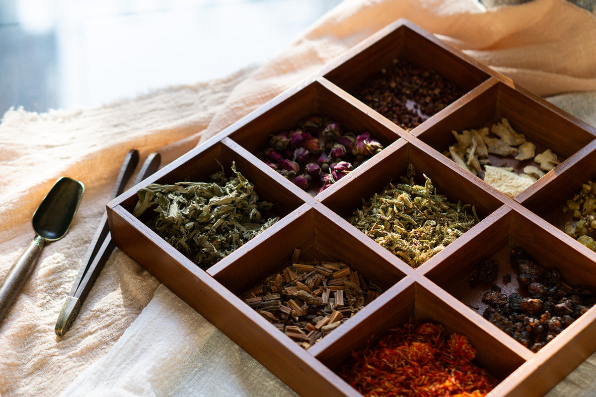 An assortment of dried botanical ingredients arranged in a wooden tray, showcasing the natural components used in a herbal foot soak ritual.