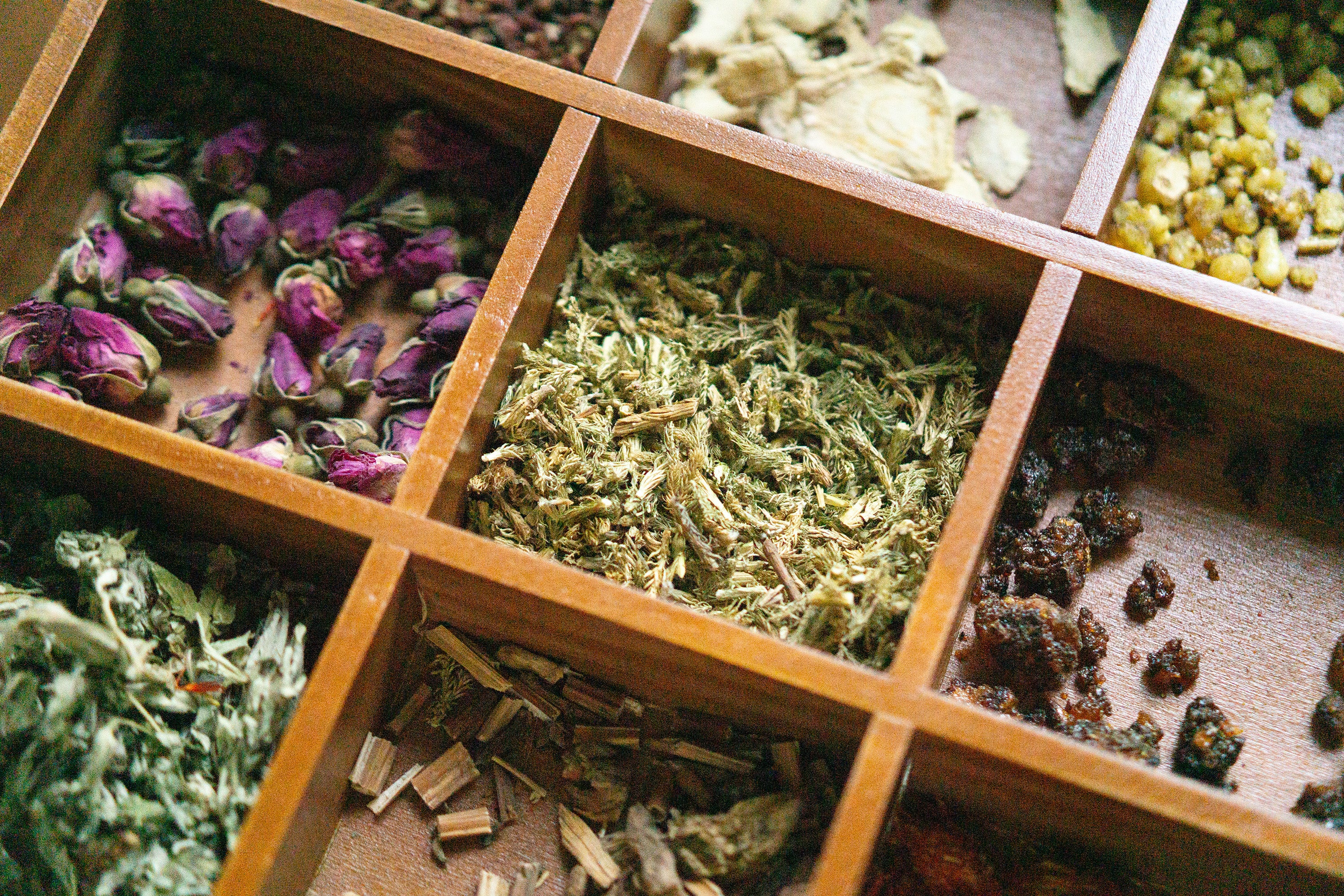Close-up of dried botanical ingredients arranged in a wooden compartment tray, highlighting natural textures and varied plant materials.