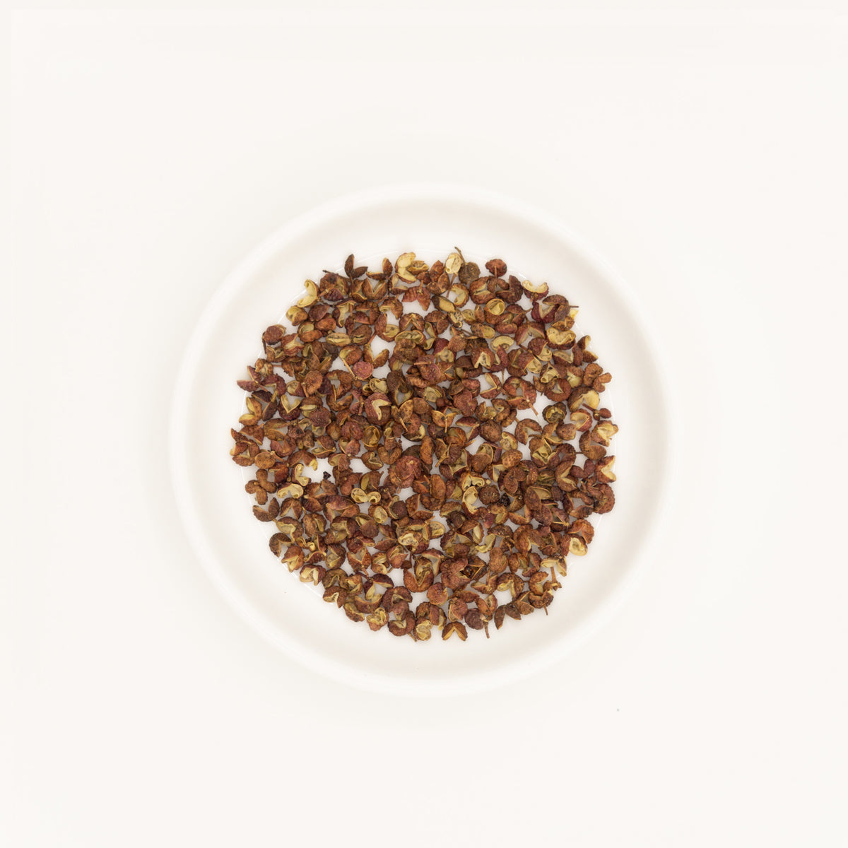 Sichuan Pepper (Zanthoxylum bungeanum) – Chinese traditional medicine (TCM) herb in white ceramic dish, white background flat lay studio photograph