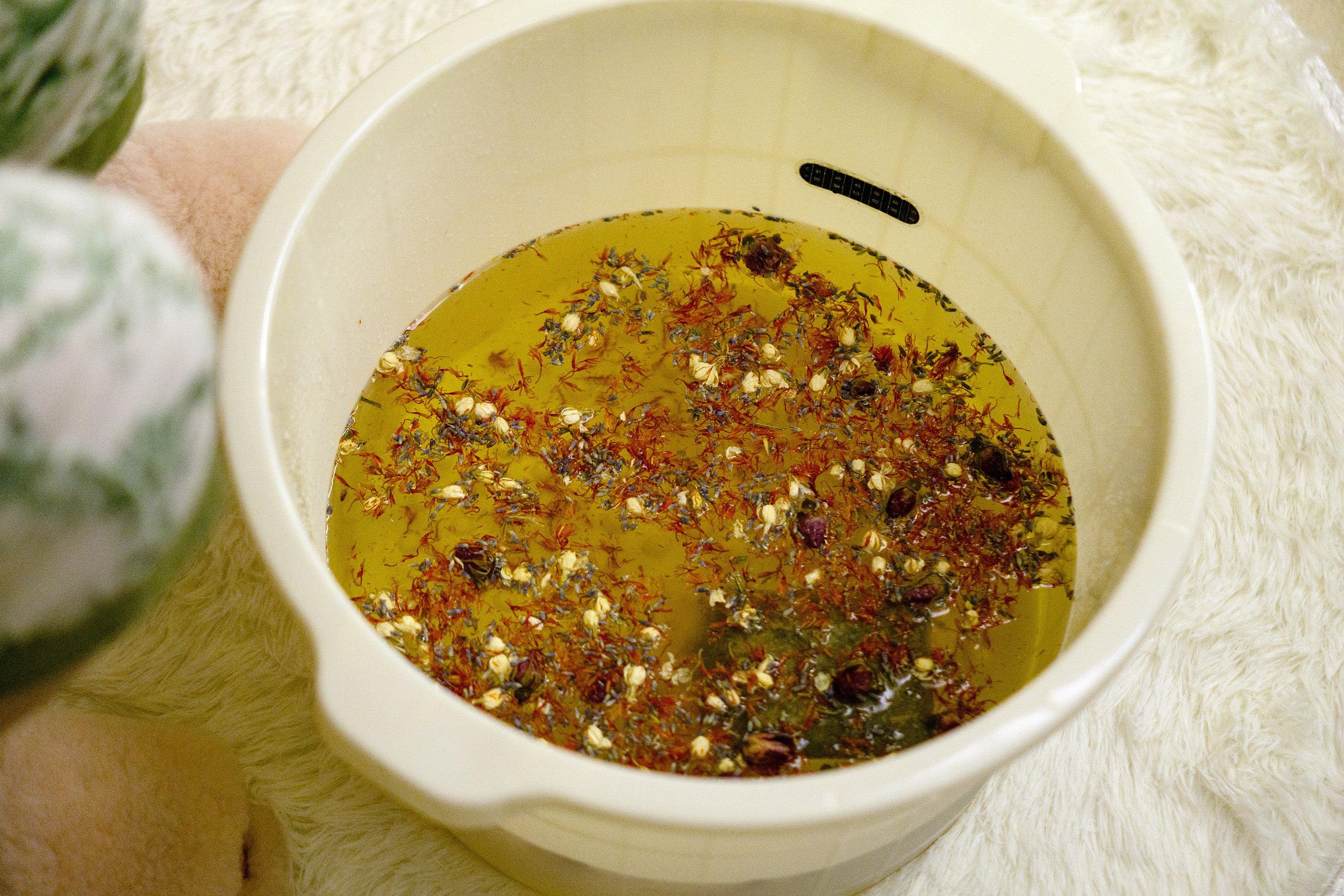 A basin filled with warm water and botanical ingredients resting before use, showing the step of allowing the water temperature to cool to a comfortable level.