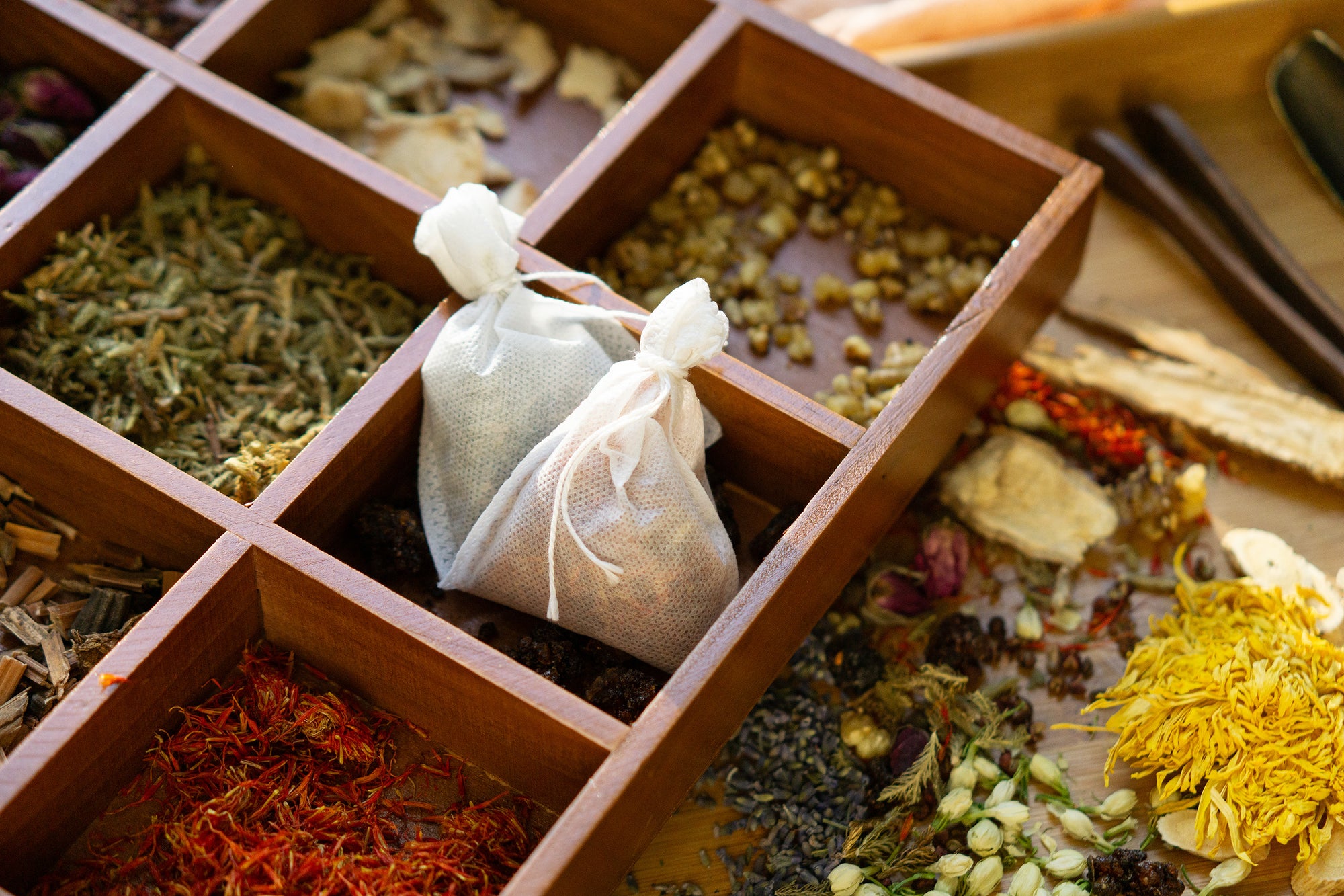 Herbal bags and various dried herbs in a wooden compartmentalized box.