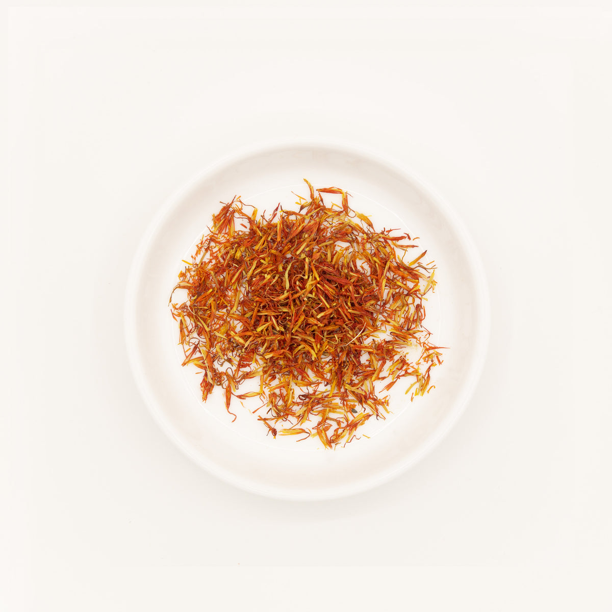 Safflower (Carthamus tinctorius) – Chinese traditional medicine (TCM) herb in white ceramic dish, flat lay white background studio photograph